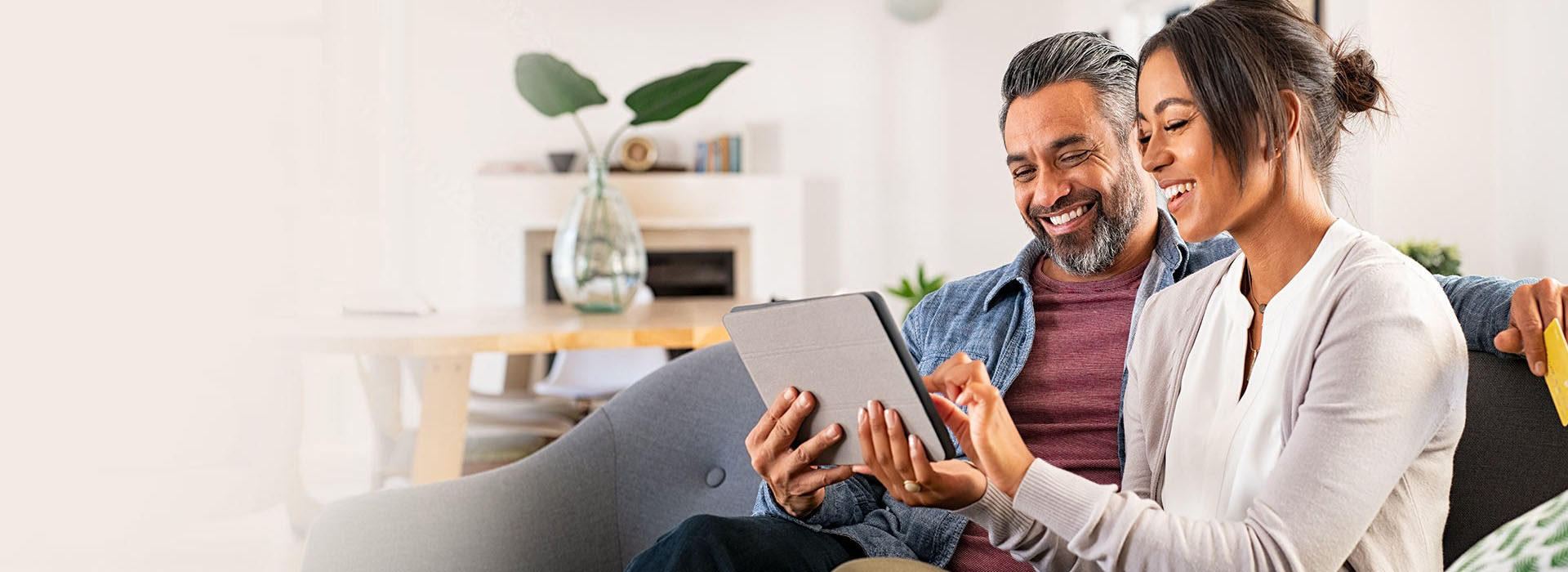 Smiling couple sitting on a sofa looking at a tablet device